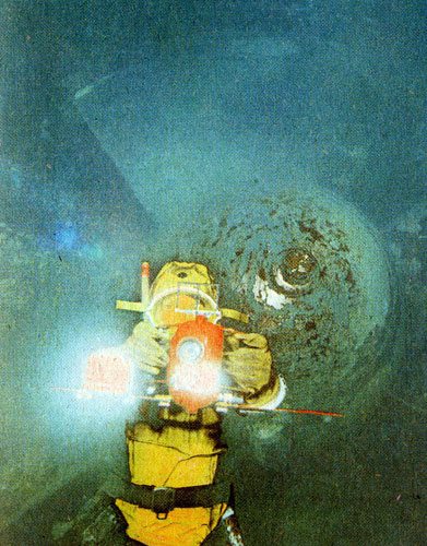 Обследование проточной части блока ПЭС под водой сопряжено с трудностями: внутри бетонного туннеля сплошной мрак, и только лампа вспышка вскрыла его тайны. Рядом с аквалангистом - лопасти турбины